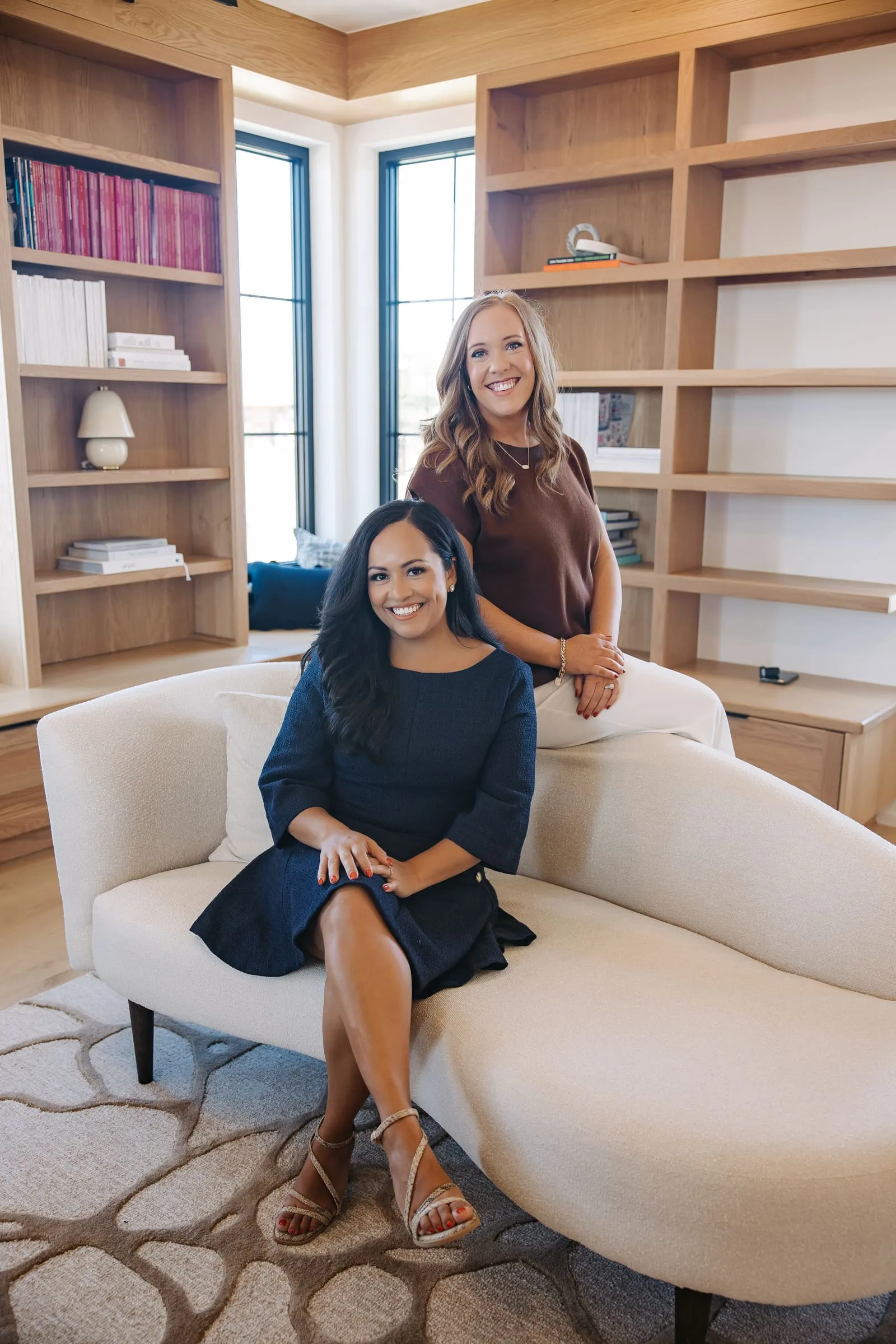 Kendra Madewell (standing, in brown) with a fellow Northwest Arkansas real estate agent in a bright, book-lined living room